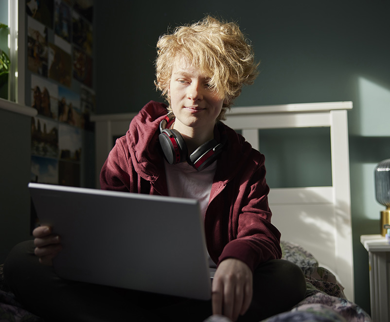 Photograph of young male using a laptop in his bedroom